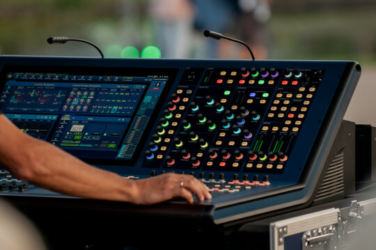 Audio engineer adjusting digital sound mixing console with colorful controls at live outdoor event, professional music production and stage management equipment in modern performance setup