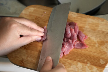 Close up of hands slicing raw meat into thin slices on a wooden cutting board with a sharp knife.