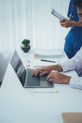 Medical Professional Focused on a Laptop: In a sterile medical setting, a doctor, engrossed in his laptop. A nurse stands in the background, holding a chart.