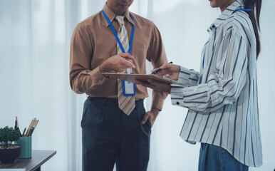 Office discussion and Sign: Professional, in office attire, engage in an intense discussion over a clipboard in a modern office setting. One individual gestures towards the document.