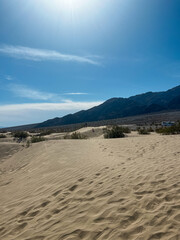 Distant view of father and two children walking on Mesquite Flat Sand Dunes under bright sun in Death Valley, USA.