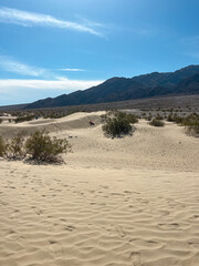 Expansive view of Mesquite Flat Sand Dunes in Death Valley with three small distant figures under a bright blue sky.