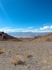 Expansive dry desert landscape in Death Valley under a bright blue sky, featuring rocky terrain and distant hills.