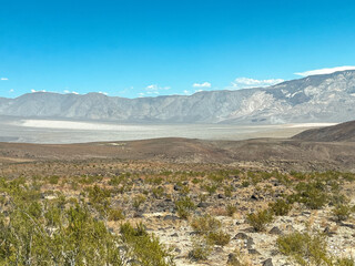 Vast dry brown Death Valley desert landscape under a clear blue sky with rocky terrain and distant horizon.
