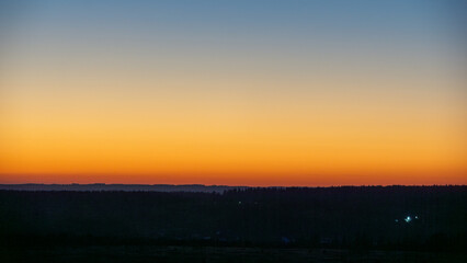 Vibrant sunset landscape showcasing a gradient of orange and blue hues over a serene horizon, with silhouettes of distant trees creating a tranquil atmosphere in nature