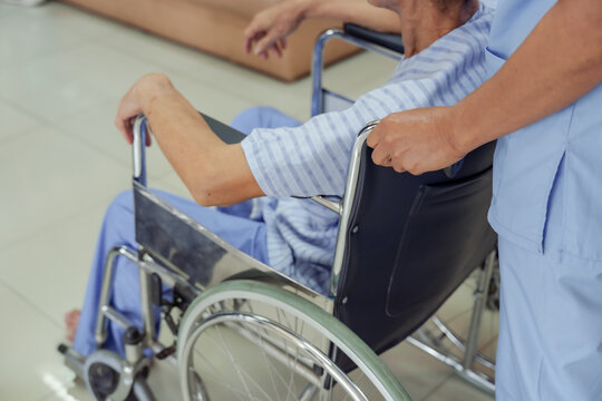 Close up view of elderly male patient sitting in wheelchair holding metal frame being transported by medical team inside hospital during recovery treatment process representing healthcare support