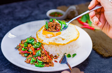 Asian food, Hands using spoon the action of picking up rice topped with stir-fried beef and basil for eat, famous street food in Thailand, fast food, soft focus