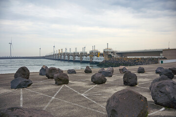 A stunning storm surge barrier, deltawerke, (neeltje jans) with large rocks in the foreground and wind turbines in the background. A technical marvel in Netherlands, Zeeland, Renesse.