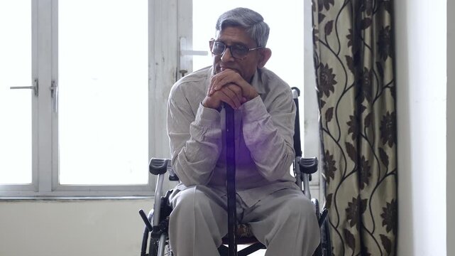 Pensive sad elderly indian man on wheelchair feel lonely in house alone. Retired disable male lost in thoughts. Handicapped Depressed Senior person Solitude and mental health concept. 4k
