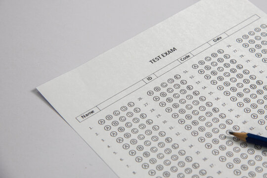 Here is a description of the image in English:

This is a close-up, angled shot of a paper multiple-choice answer sheet, often called a "bubble sheet." It shows numbered questions down the side (1, 2,