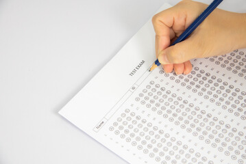 The image shows a hand holding a pencil and filling in a multiple-choice answer sheet for a test....