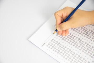The image shows a hand holding a pencil and filling in a multiple-choice answer sheet for a test....