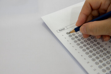 The image shows a hand holding a pencil and filling in a multiple-choice answer sheet for a test....