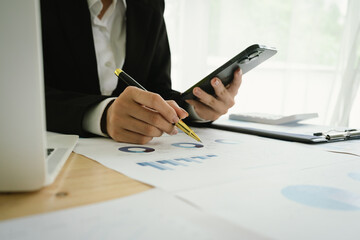 Fototapeta premium A business professional analyzes colorful financial charts and graphs on a desk, holding a pen and clipboard, representing planning, strategy, performance, and project management in the workplace.