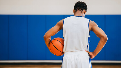 Ready Basketball Player - Focus and Determination, A male basketball player in a white uniform holds an orange basketball, poised on a basketball court.