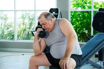 An overweight man is lifting dumbbells while working out at the gym as part of his weight loss exercise routine.