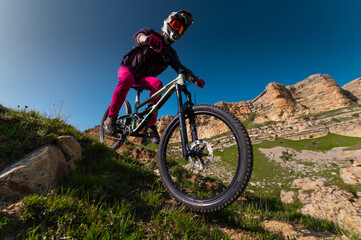 Naklejka premium Mountain biker riding down a grassy slope. Enduro mountain bike. MTB against a mountain landscape
