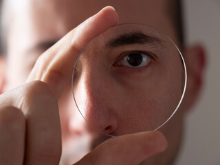 Optician looks through a glass lens. Eye care professional optometrist doctor man holding a glass lens inside laboratory