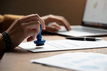 Fototapeta premium Person using a blue stamp on a document with a laptop and pen in the background on a desk