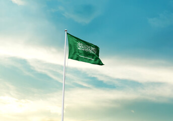 Saudi Arabia flag is waving on a tall flagpole among the clouds. Saudi Arabian national flag for independence day.