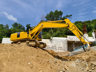 A large yellow excavator is currently positioned on top of a huge pile of dirt