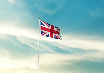 United Kingdom flag is waving on a tall flagpole among the clouds. UK national flag for...