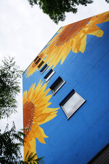 artistically painted house, skyscraper reaching for the sky, with huge sunflower blossom on blue...