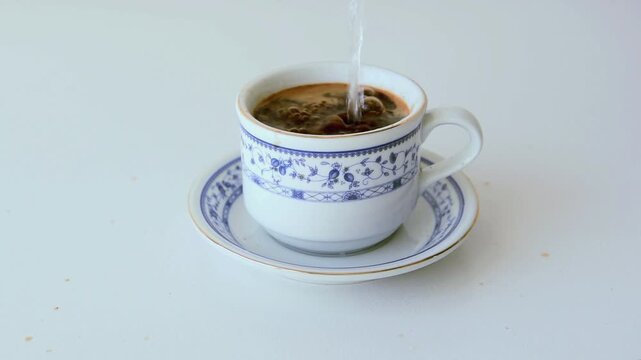 Pouring hot water into coffee in an oriental style cup, until the coffee overflows and wets the table