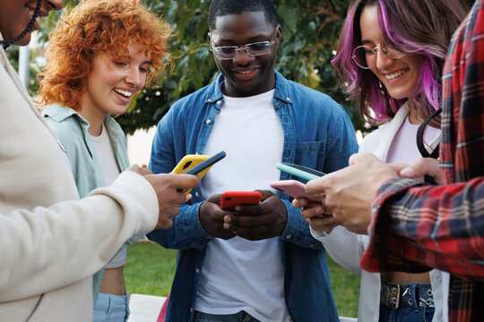 Group of diverse students using smartphones together outdoors - Powered by Adobe