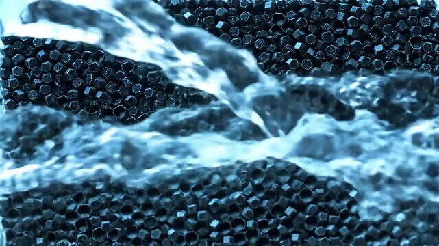 Water pours over a bed of tiny dark polyhedral objects in a close-up view