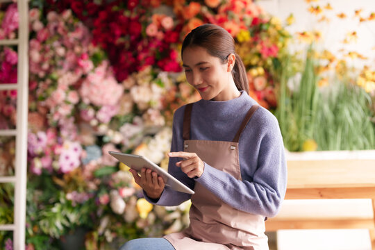 Asian adult florist managing flower shop inventory sales using digital tablet modern retail business operations beautiful floral display - Powered by Adobe