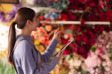 Asian female florist uses digital tablet managing flower shop business modern retail operations for efficient floral inventory and customer service