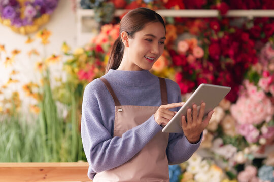 Asian female adult florist managing flower shop business using tablet modern digital technology retail operations happy entrepreneur blooming success - Powered by Adobe