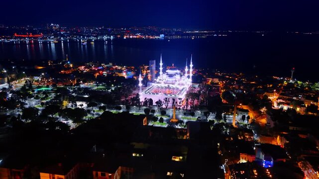 Distancing from a beautiful luminous mosque in the panorama of Istanbul. Drone footage over the night city with street lights on.