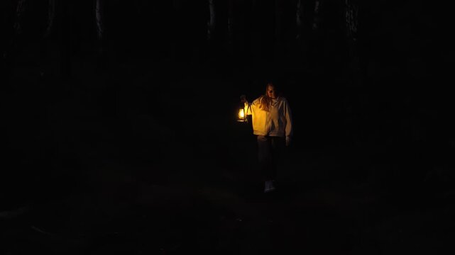 A lonely, anxious woman walks through the forest at night with a burning kerosene lamp in her hand. The concept of anxiety, arousal and fear.