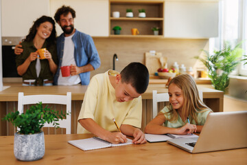 Children doing homework in kitchen while parents having breakfast