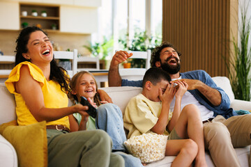 Obraz premium Happy family watching comedy on tv and laughing together on sofa