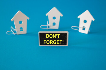 Do not Forget symbol. Wooden houses stay next to a wooden black board with the words Don't Forget. Beautiful blue background. Business and Reminder Note concept
