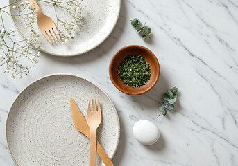 minimal table setting with wooden cutlery and herbs on marble surface

