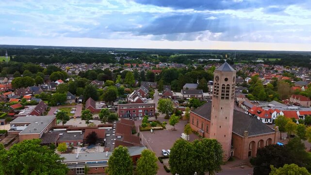 Green panorama of modern Vierlingsbeek, Netherlands. Footage near the brick clock tower of Saint Lawrence Church. Sun beams go through the clouds in the sky.