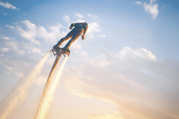 A flyboard athlete hovers over the water against the sunset sky, propelled by powerful jet streams...