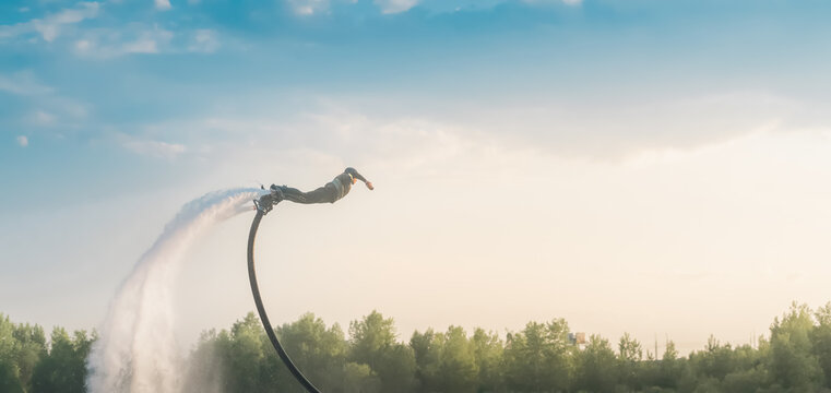 A man on a skateboard flies over the water like a superhero. Extreme sports.