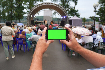 Man recording open air classical music concert with smartphone showing green screen