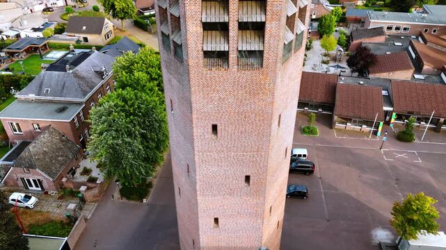 Rise along the brick tower with clock. Church in Vierlingsbeek, Netherlands. Green residential area at backdrop.