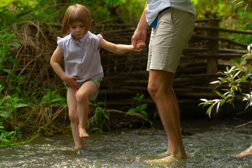 A little girl is happily gripping a mans hand as they carefully cross a flowing river together, enjoying the moment outdoors