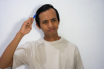  A young Asian man scratching his head with a comb with a confused and thoughtful expression.