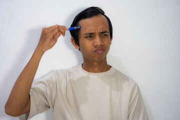  A young Asian man scratching his head with a comb with a confused and thoughtful expression.