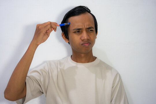  A young Asian man scratching his head with a comb with a confused and thoughtful expression.