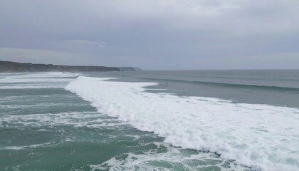 Fototapeta premium Expansive ocean view; rolling waves break near a coastline under a cloudy sky