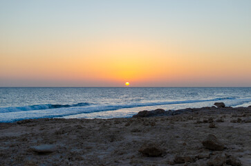 Sunset over the sea with orange sky and beach rocks in Egypt